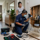 Professional plumber detecting hidden pipe leak behind wall in Malaysian home with visible water damage stains and inspection tools.